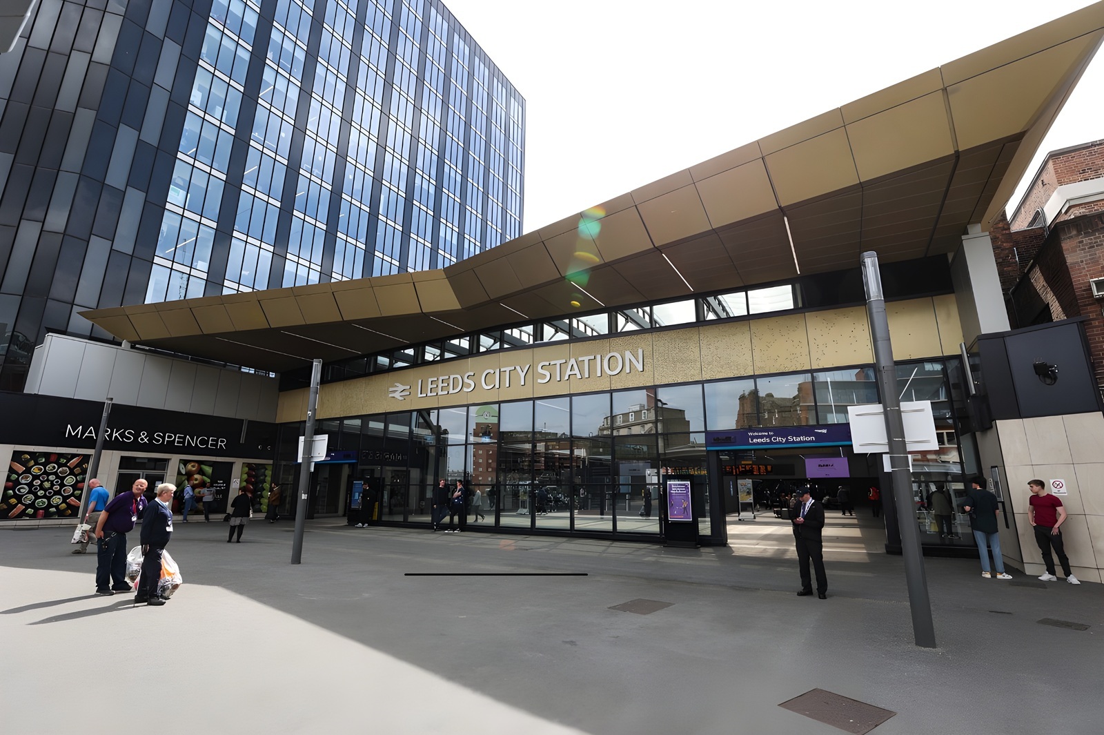 Outside view of Leeds City Station with security guards and travelling people coming in and out of the station. Perfect opportunity for people looking for shops to let in Leeds.