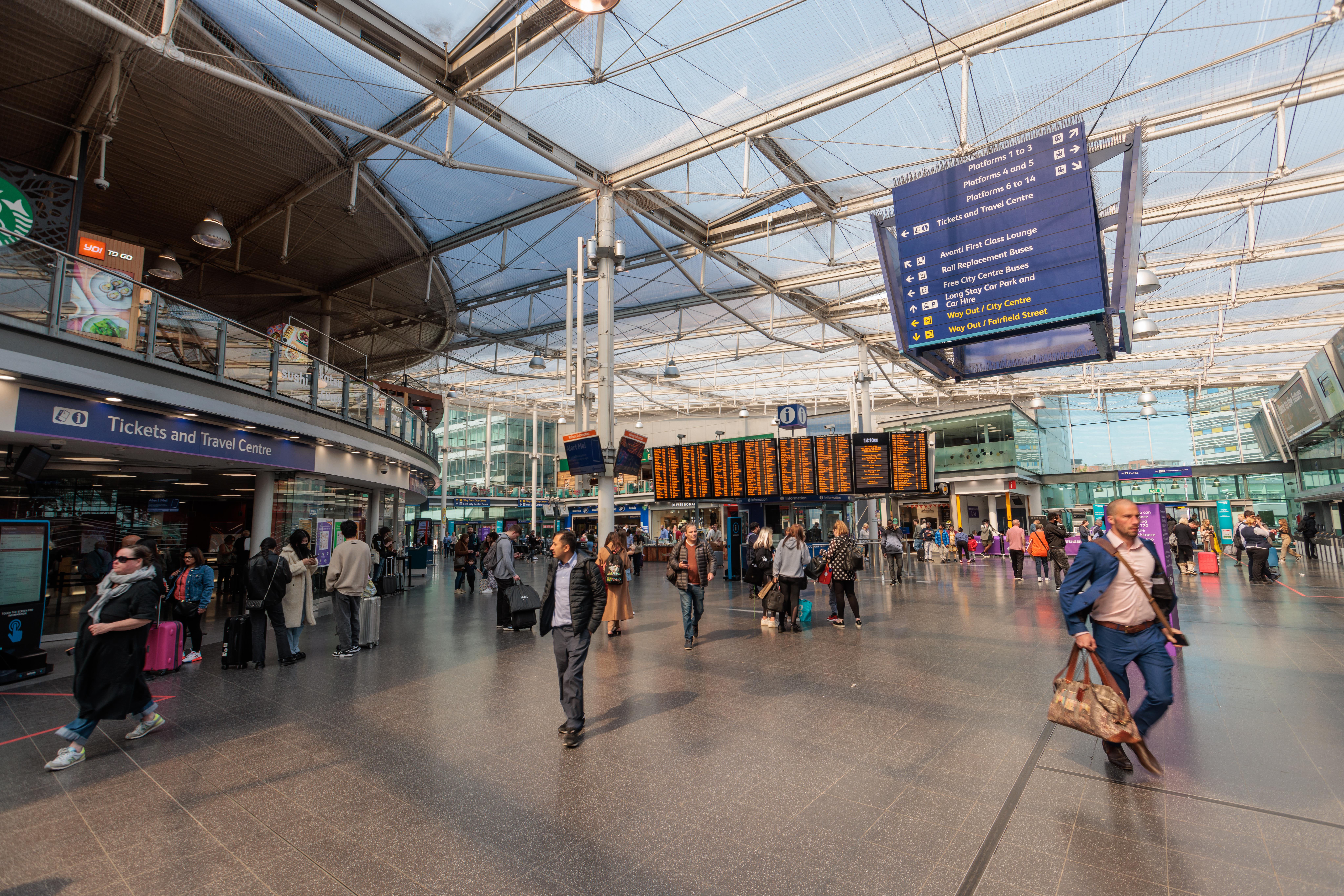 Crowd of passengers moving through a station concourse with retail outlets.
